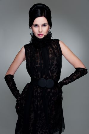 attractive young brunette in black dress posing against grey backgroundの写真素材