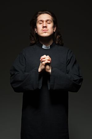 young priest is praying against dark backgroundの写真素材