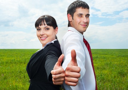 smiley businesspeople showing thumbs up over green grass and blue skyの写真素材