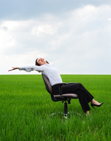 happy businesswoman resting on chair over green meadowの写真素材