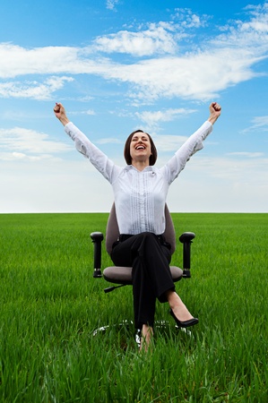 happy businesswoman sitting on chair over green meadow の写真素材