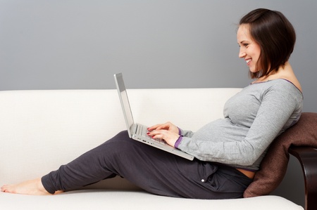 cheerful pregnant woman with laptop sitting on sofaの写真素材