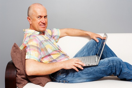 elderly man with laptop on sofa at homeの写真素材