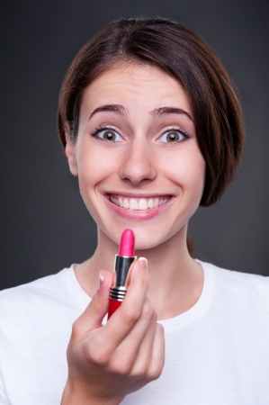 joyous young woman holding lipstick and smiling. studio shot over dark backgroundの写真素材