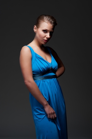 alluring young female in blue dress posing over dark backgroundの写真素材