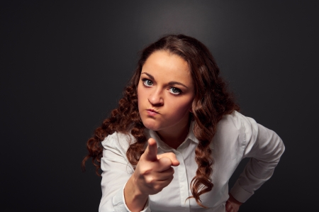 studio shot of angry woman pointing at camera. picture over dark backgroundの写真素材