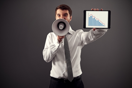 emotional businessman showing the business graph and shouting with megaphone against grey background
の写真素材