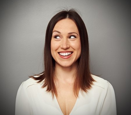 cheerful young brunette looking at something over dark backgroundの写真素材