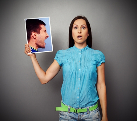 startled young woman holding photo of aggressive manの写真素材