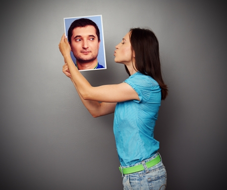 young woman kissing the picture of young man over grey backgroundの写真素材