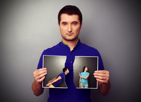 serious man holding the lacerated photo of young couple in quarrelの写真素材