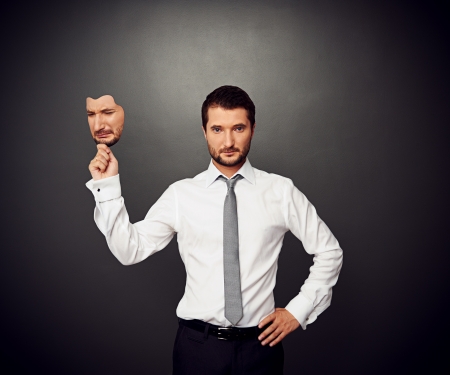 serious businessman holding mask with crying faceの写真素材