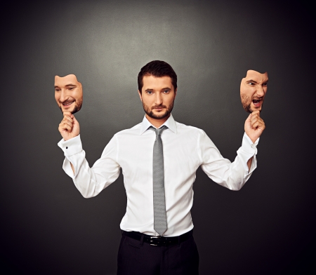 serious businessman holding two masks with different moodの写真素材