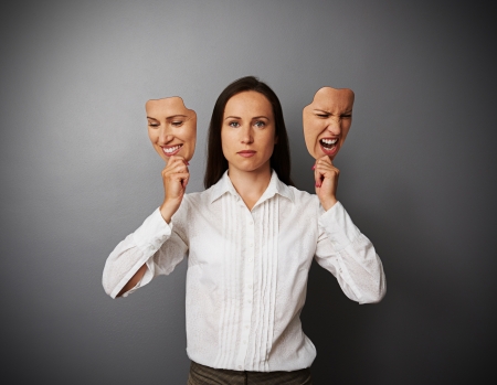 serious woman holding two masks with different moodの写真素材
