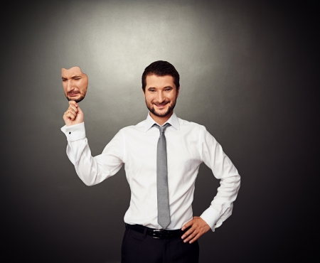 smiley businessman holding sad mask over dark backgroundの写真素材