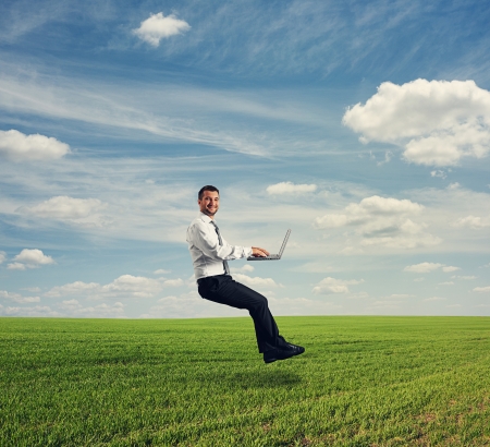 successful businessman working with laptop and hover over green fieldの写真素材