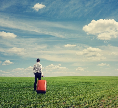 back view of businessman with suitcase standing on the green fieldの写真素材