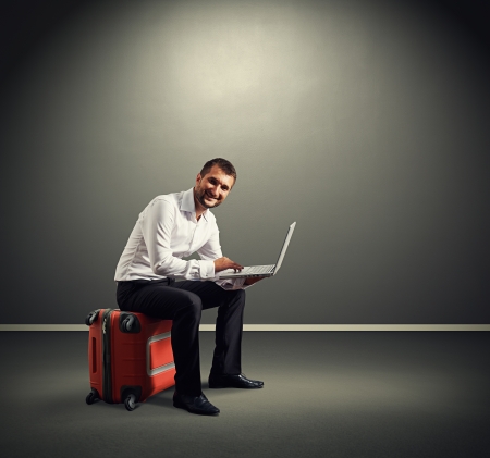 smiley man sitting on the suitcase and working with laptopの写真素材