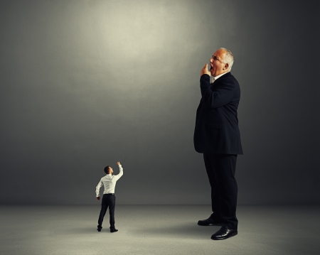 small man showing fist to big yawning businessmanの写真素材