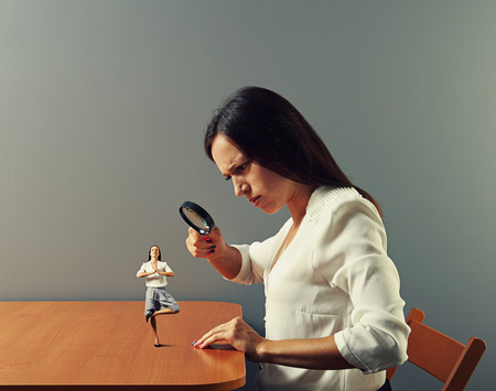 serious businesswoman looking with magnifying glass at small meditation womanの写真素材