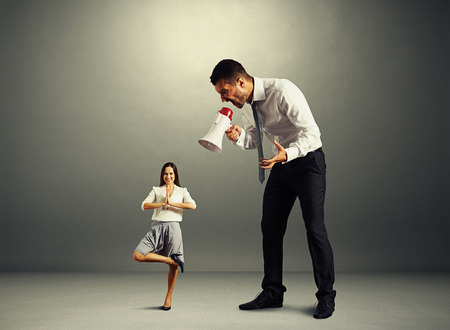 aggressive boss screaming at small calm woman over dark backgroundの写真素材