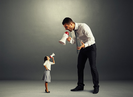 quarrel between small woman and big man over dark backgroundの写真素材