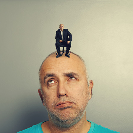 weary senior man with small businessman on his headの写真素材