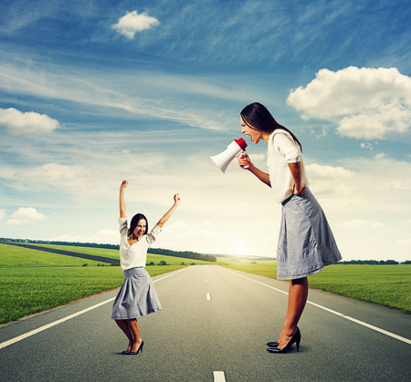 angry woman with megaphone and small happy woman at outdoorの写真素材