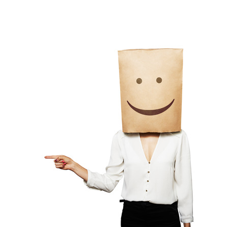 woman with smiley paper bag on the head pointing at something over white backgroundの写真素材