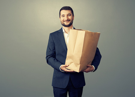 smiley businessman holding paper bag over dark の写真素材