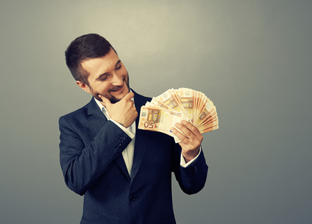smiley businessman looking at money and thinking about something over dark の写真素材