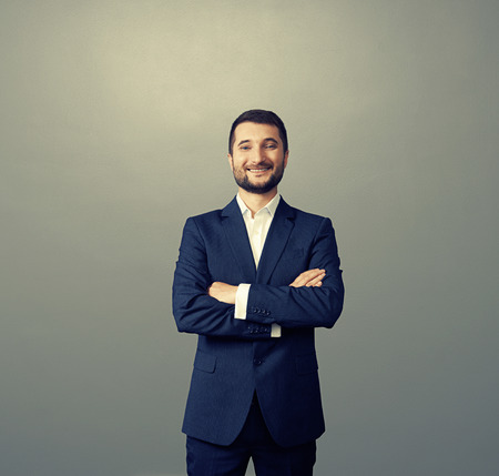 handsome businessman with folded hands over dark background