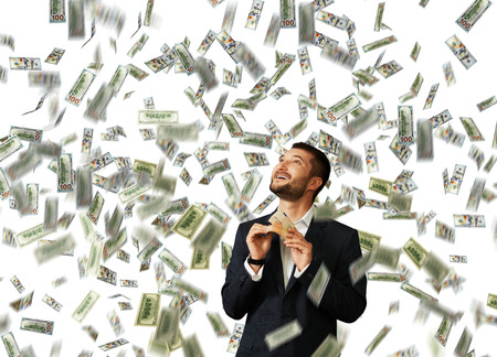 laughing happy man standing under dollar's rain, holding money and looking upの写真素材