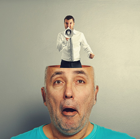 amazed senior man with screaming young businessman in the head over grey backgroundの写真素材