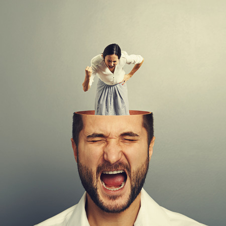stressed shouting man with open head. young angry businesswoman standing into the head, looking at the man and screaming. photo over grey backgroundの写真素材