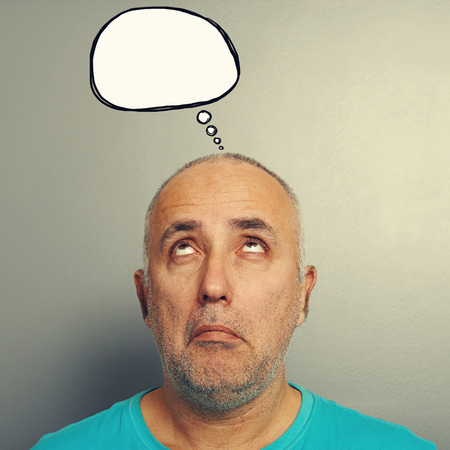 portrait of pensive senior man looking up at empty speech bubble over grey backgroundの写真素材