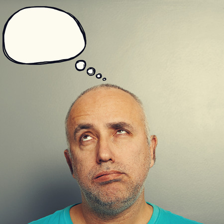 portrait of bored senior man looking up at speech bubble over grey background