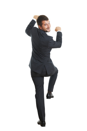 back view of businessman in formal wear climbing up on white wall, turning round, looking at camera and smiling. isolated on white backgroundの写真素材