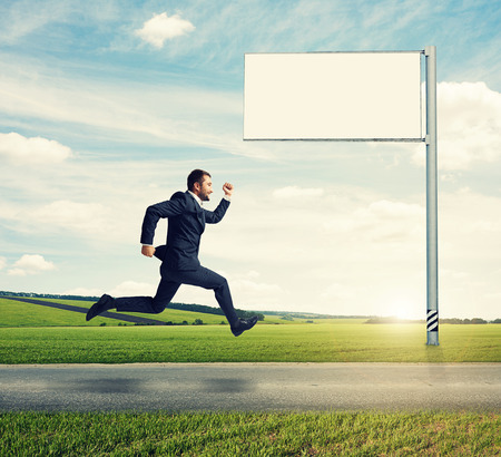 successful businessman running on the road against empty billboard and green fieldの写真素材