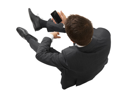 view from above of businessman in black suit with cellphone sitting on the floor. isolated on white backgroundの写真素材