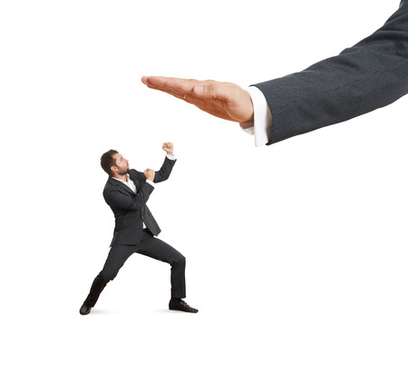 concept photo of conflict between subordinate and boss. angry young businessman showing fist and looking up at big palm of his boss. isolated on white backgroundの写真素材