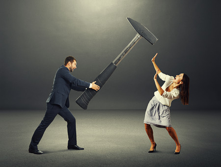 angry screaming man holding big hammer and hitting scared woman. photo in the dark roomの写真素材