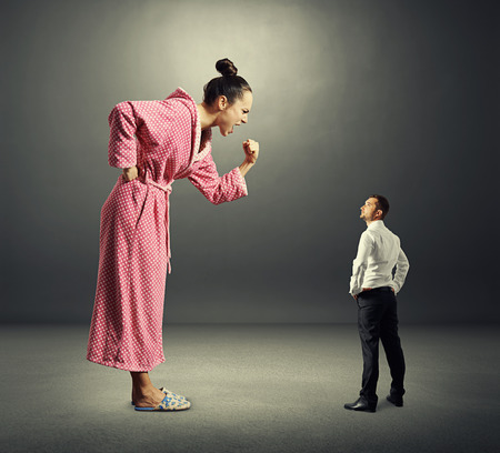 small serious man in black suit looking at big angry woman in pink dressing gown. photo over dark backgroundの写真素材