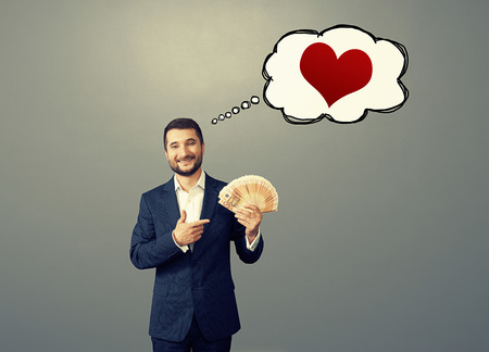 smile businessman pointing at paper money and thinking about love over grey backgroundの写真素材