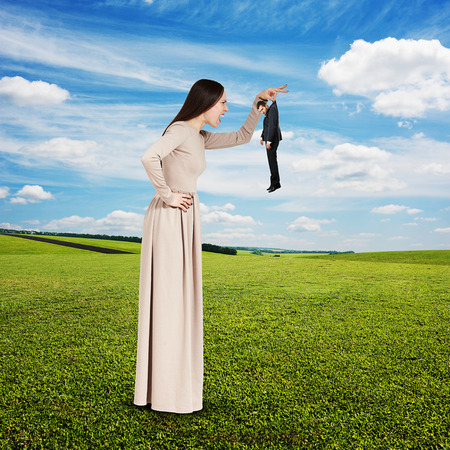 yelling young woman with small man over green field and blue skyの写真素材