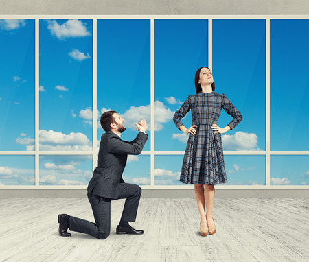 sad man looking at young attractive woman and asking for forgiveness. photo in empty room with big windowsの写真素材