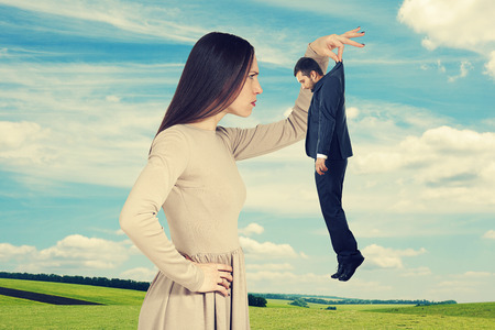 serious young woman looking at small man over sky and green fieldの写真素材