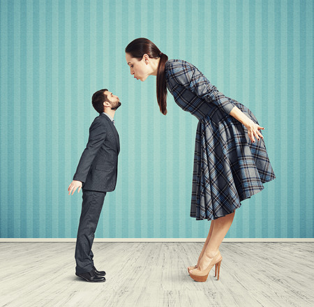 big woman kissing small man. couple in empty room with blue wallの写真素材