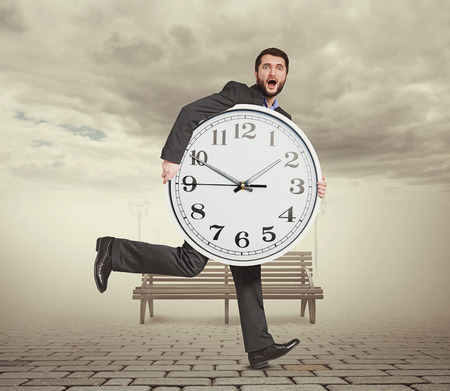 startled man holding big clock and running in foggy parkの写真素材
