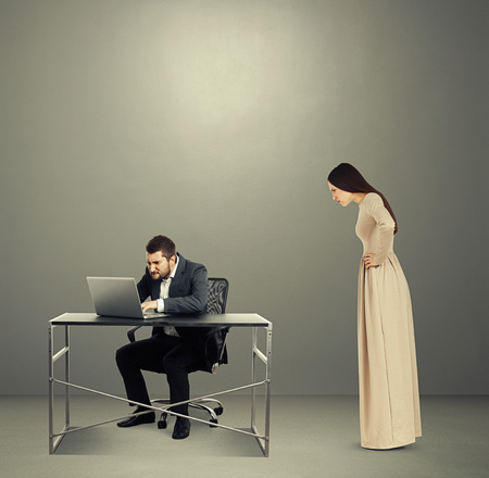 concentrated man looking at laptop, angry woman staring at man. photo in dark roomの写真素材